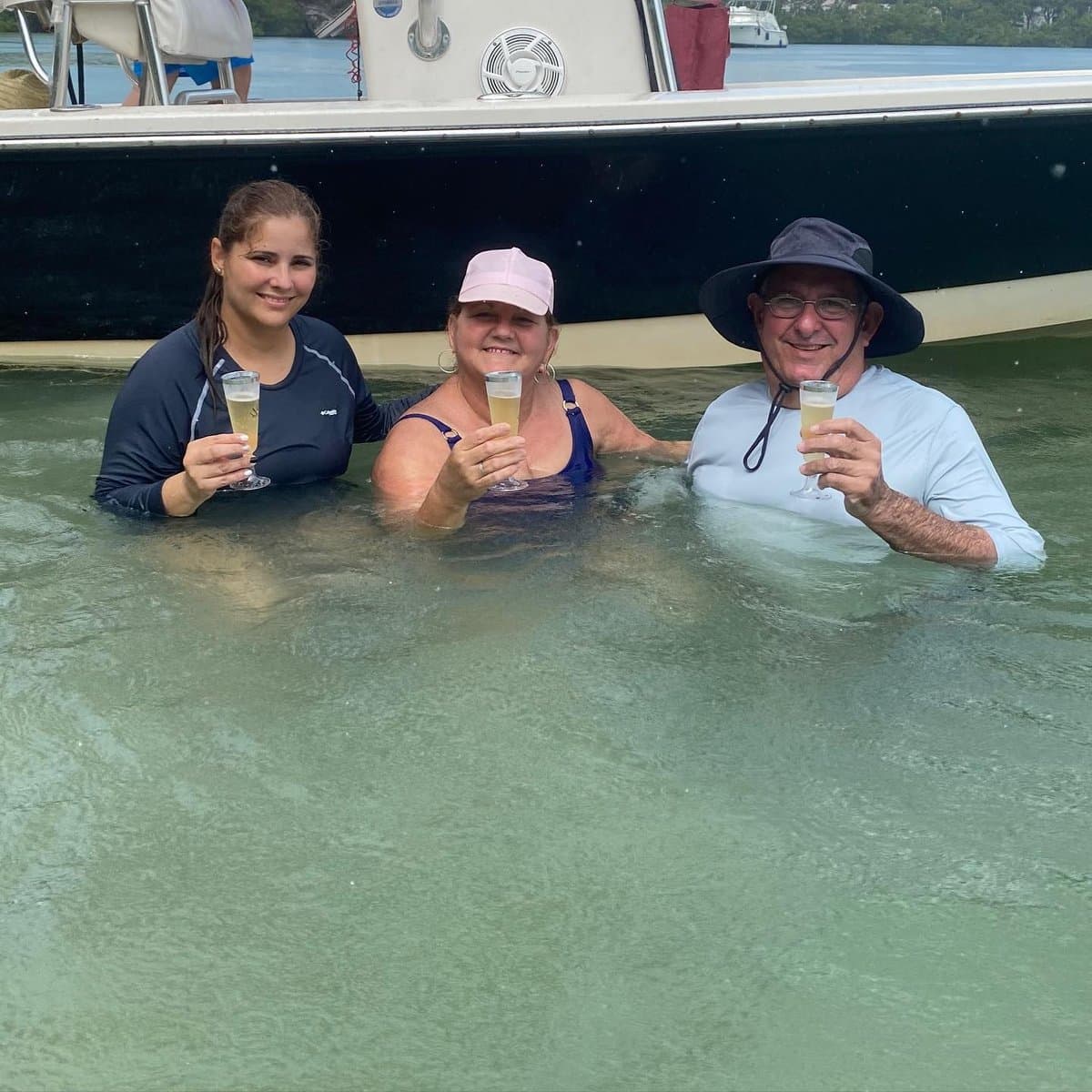 Three guests toasting with champagne in the shallow sandbar water beside the boat