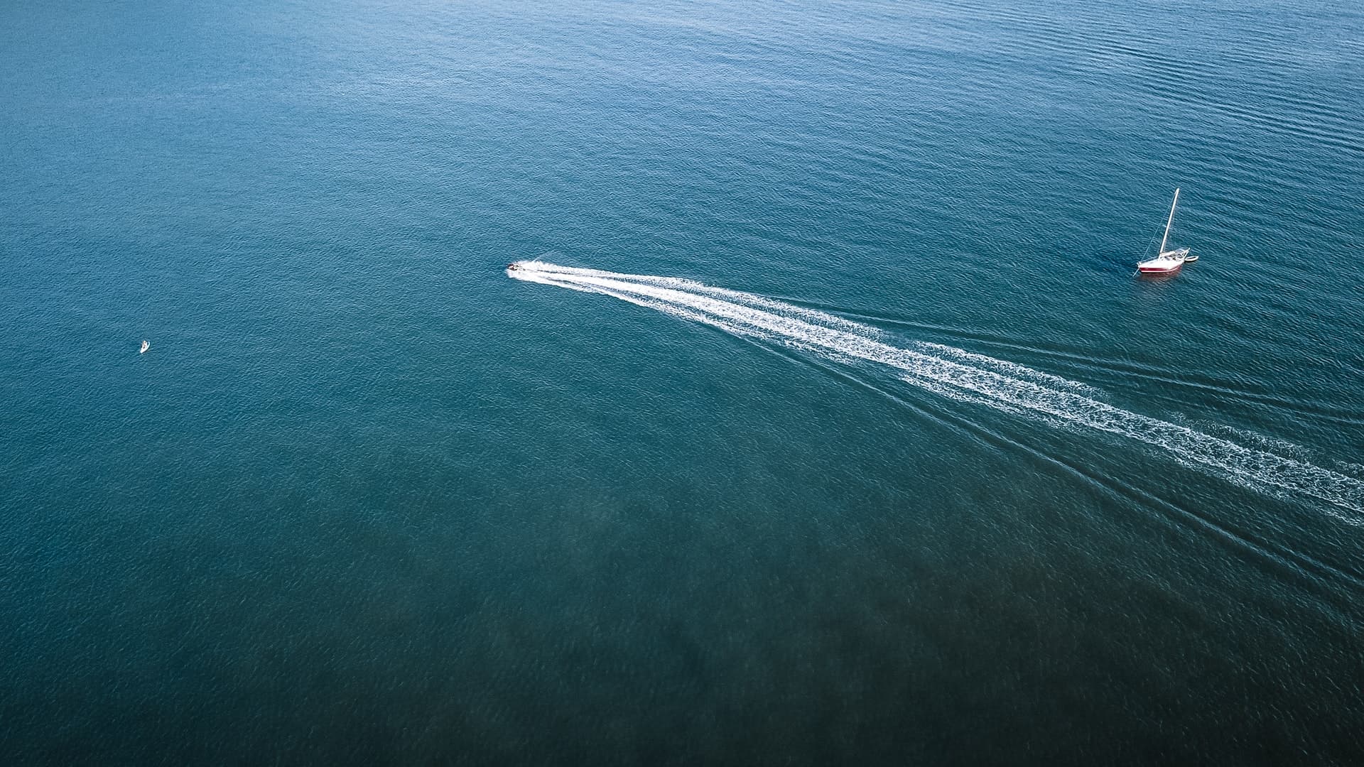 Aerial view of a boat cutting a white wake across deep blue water